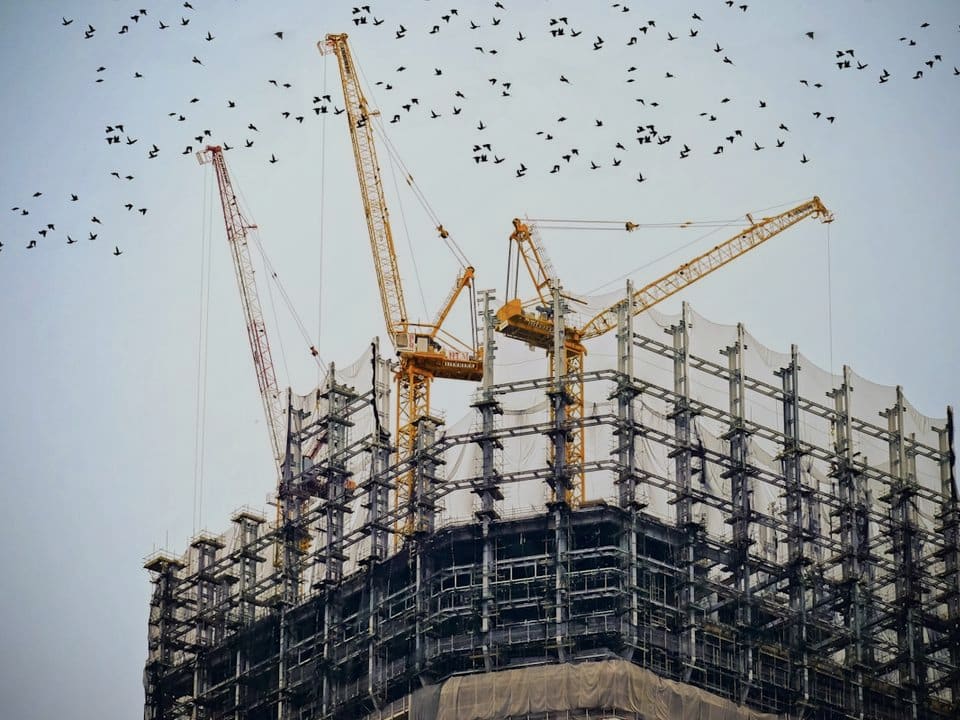 Tower cranes over a building wrapped in scaffolding