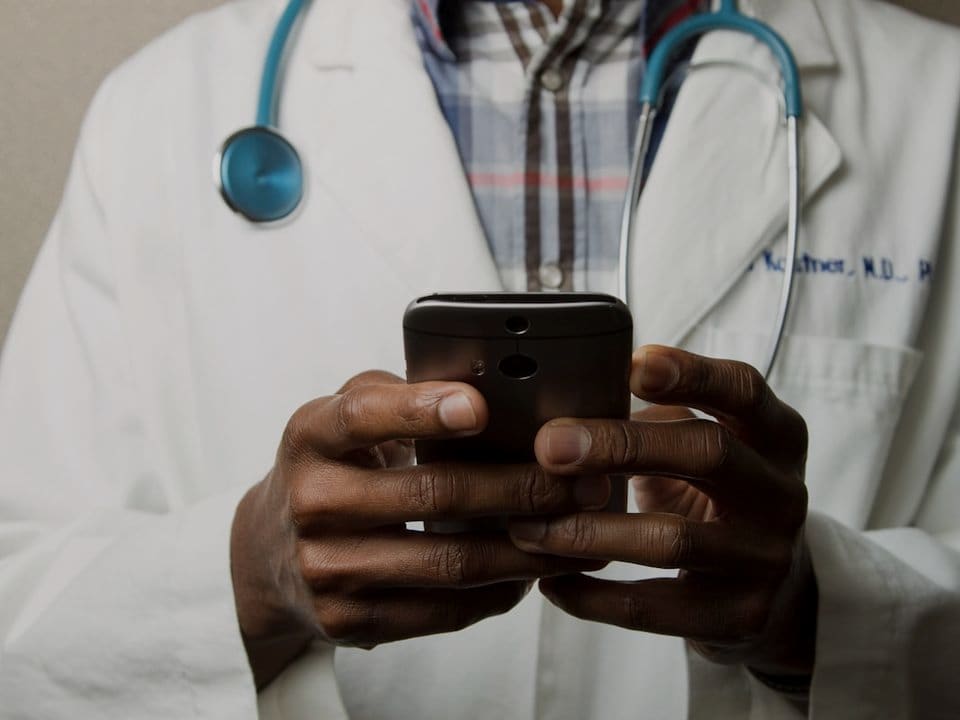 A physician with a stethoscope reviewing messages on a phone